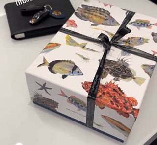 Estuche blanco con peces dibujados en acuarelas que guarda en su interior dos botellas de vino submarino Crusoe Treasure. El estuche está rodeado de un lazo de regalo. 